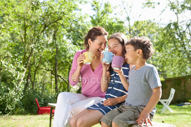 Madre e hijos bebiendo en el banco - foto de stock