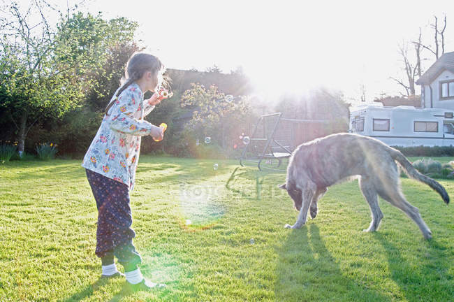 Chica soplando burbujas con perro - foto de stock