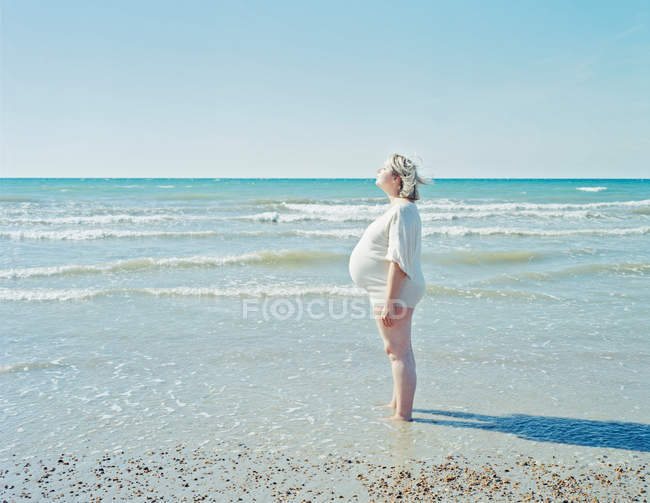 Беременная женщина стоит на пляже — стоковое фото