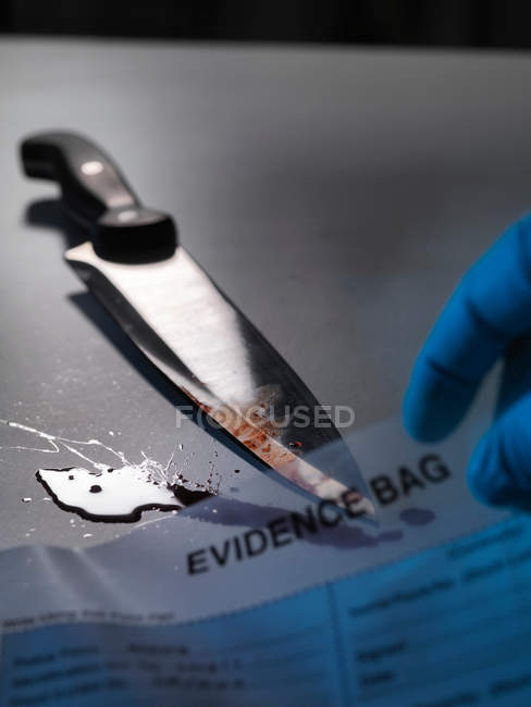 Cuchillo y mano sosteniendo bolsa de evidencia - foto de stock