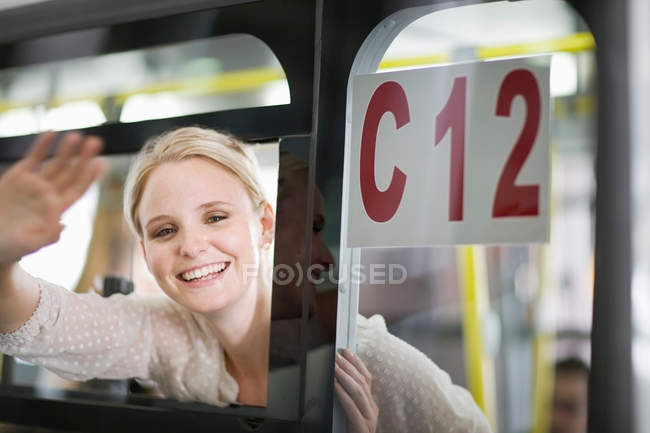 Mujer saludando adiós desde la ventana - foto de stock