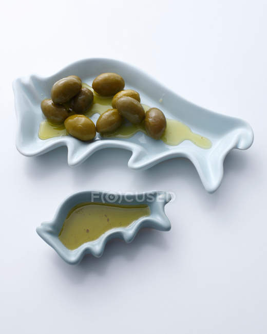 Aceitunas verdes y aceite de oliva en platos - foto de stock