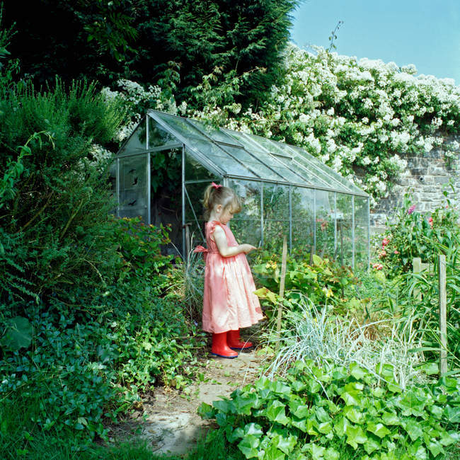 Girl playing in garden by greenhouse — Stock Photo