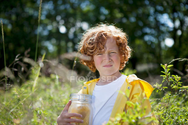 Menino segurando frasco no campo de grama alta — Fotografia de Stock