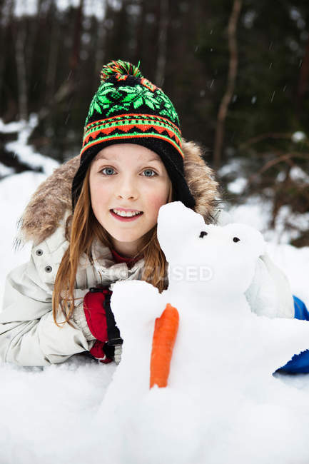 Fille souriante jouer avec bonhomme de neige — Photo de stock