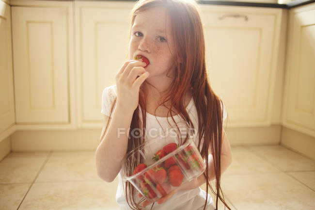 Fille manger fraise sur le sol de la cuisine — Photo de stock