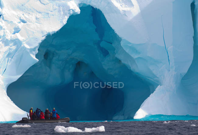 Лодка с людьми, плавающими возле айсберга — стоковое фото