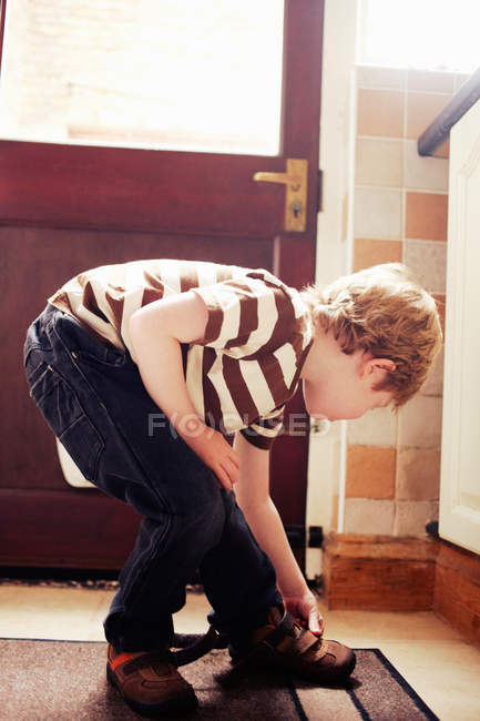 Мальчик вяжет ботинки у двери — стоковое фото