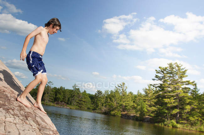 Ragazzo che si arrampica sulla roccia lungo il fiume — Foto stock