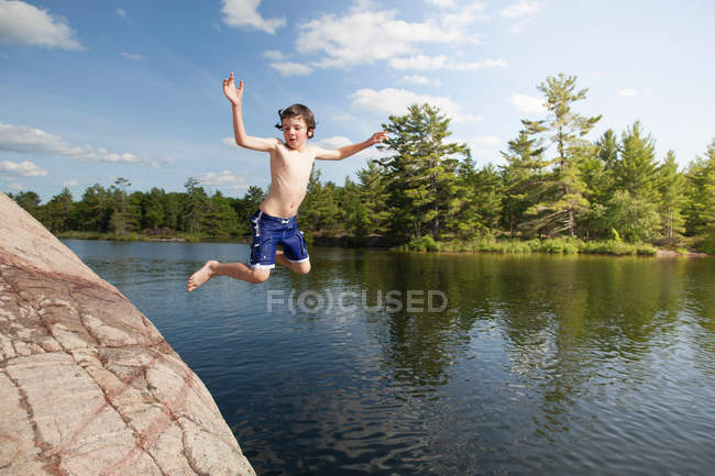 Boy jumping into still lake — Stock Photo