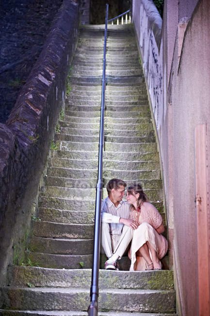 Pareja sentada en las escaleras urbanas por la noche - foto de stock
