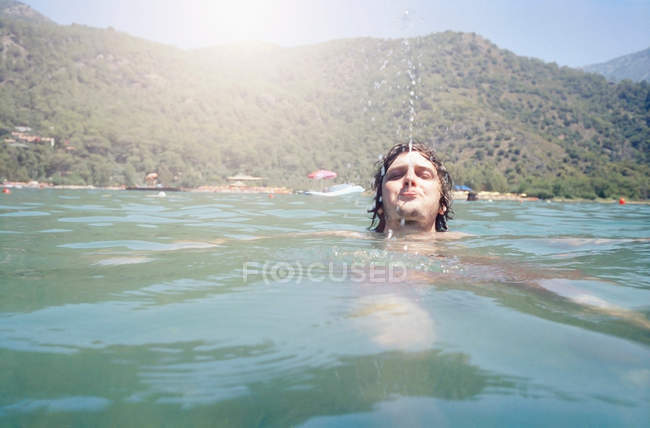Человек плавает и дует воду — стоковое фото
