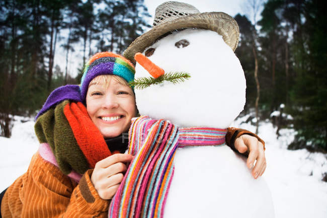 Mujer sonriente abrazando muñeco de nieve - foto de stock