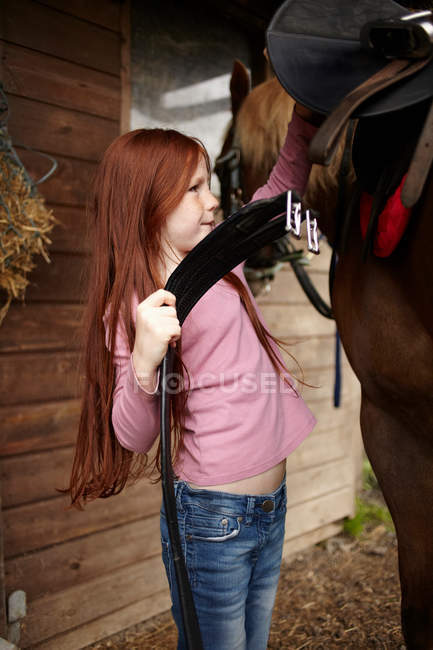 Mädchen befestigt Pferdesattel an Scheune — Stockfoto