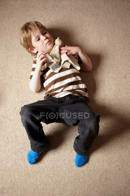 Junge liegt auf Teppich und hält Spielzeug — Stockfoto