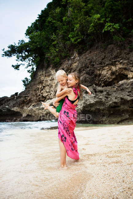Girl carrying brother on beach — Stock Photo
