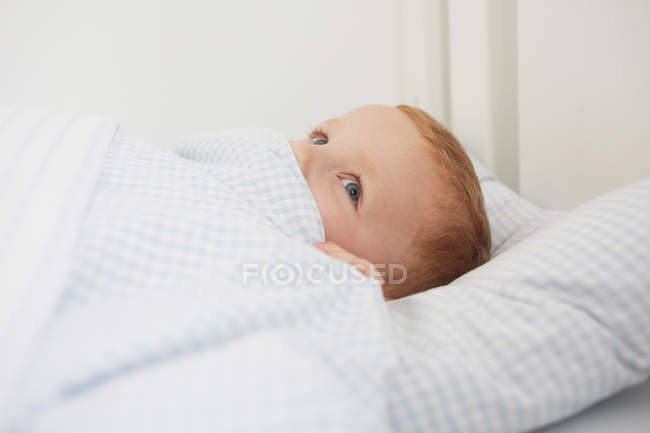 Junge versteckt im Bett und schaut weg — Stockfoto