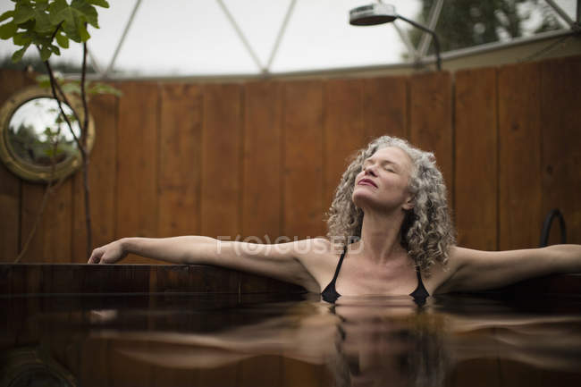 Зрелая женщина расслабляется в гидромассажной ванне на эко-ретрите — стоковое фото