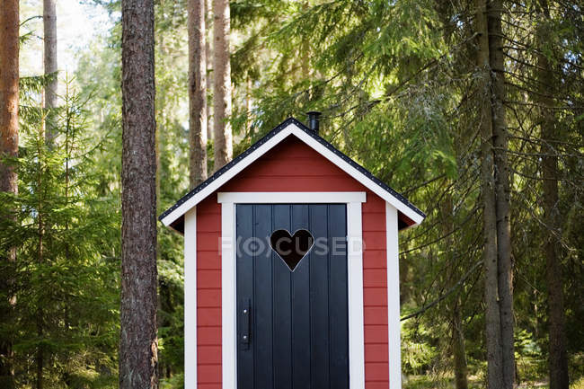 Casa pequeña cabaña en el bosque, puerta con agujero en forma de corazón - foto de stock