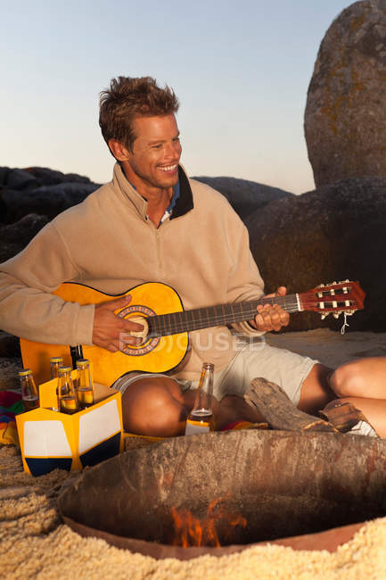 Homem tocando guitarra com cerveja na praia — Fotografia de Stock