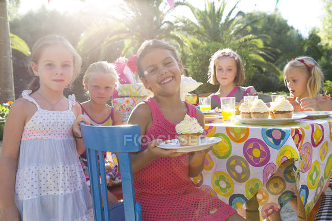 Chica en la fiesta de cumpleaños con amigos sosteniendo plato con magdalena - foto de stock