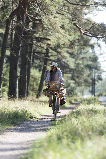 Жінка катається на велосипеді на лісовій доріжці з кошиками для їжі — стокове фото