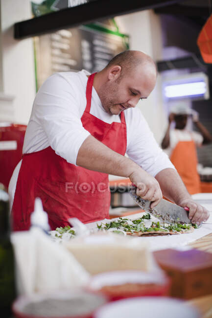 Chef slicing pizza in kitchen — Stock Photo