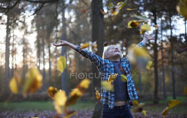 Menino feliz jogando folhas no ar — Fotografia de Stock
