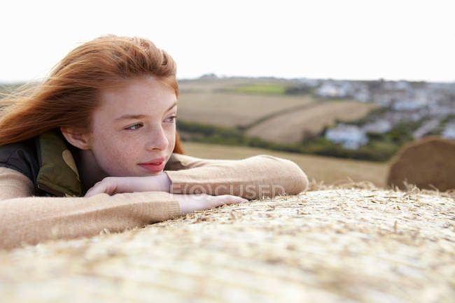 Teenage girl resting on hay bale, focus on foreground — Stock Photo