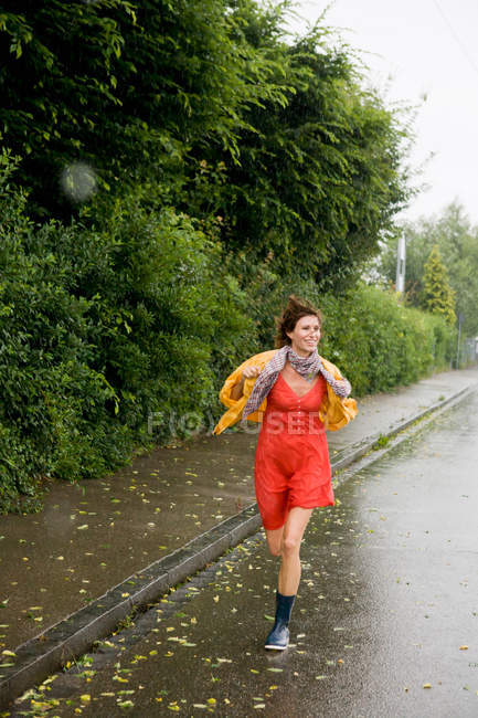 Mujer sonriente corriendo bajo la lluvia, enfoque selectivo - foto de stock