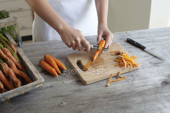 Mãos de adolescente menina descascando cenouras — Fotografia de Stock