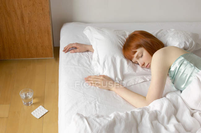 Mulher dormindo na cama com comprimidos — Fotografia de Stock
