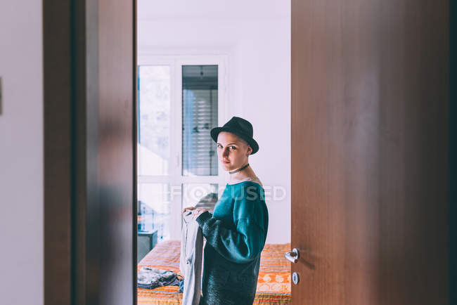 Doorway portrait of young woman wearing trilby standing in bedroom — Stock Photo