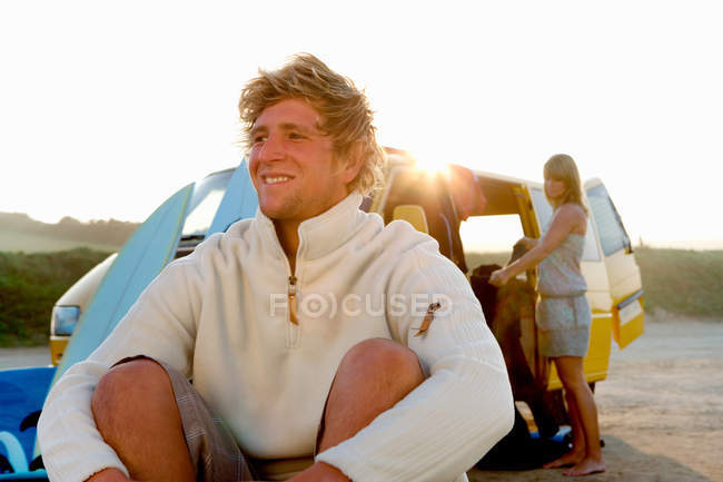 Мужчина, сидящий на пляже и улыбающийся женщине — стоковое фото