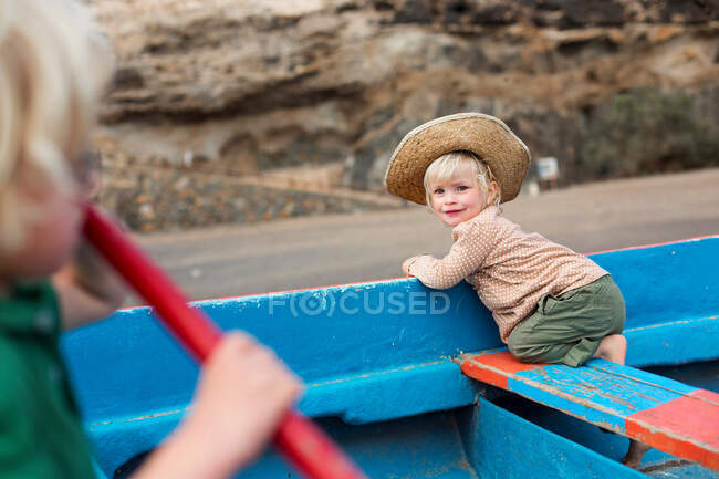 Petite fille assise dans un bateau sur la plage — Photo de stock