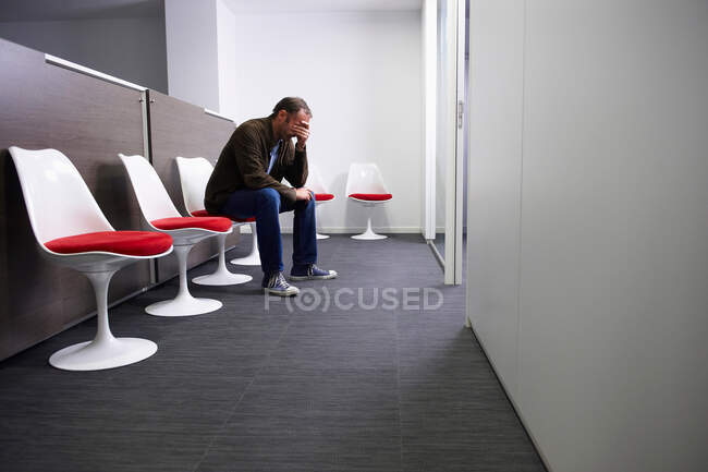 Hombre sentado en la sala de espera de un médico - foto de stock