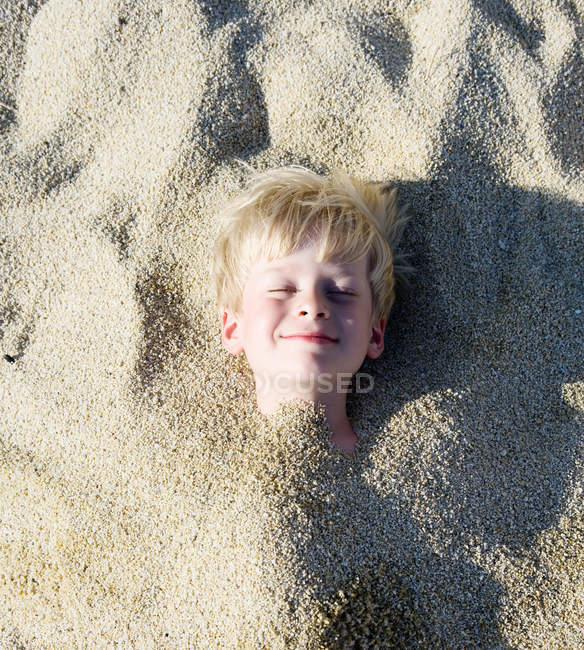 Jovem enterrado na areia sorrindo — Fotografia de Stock
