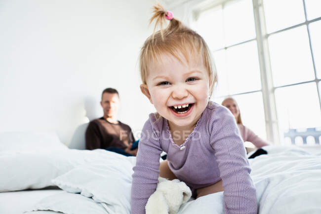 Toddler girl on parent's bed looking at camera, laughing — Stock Photo