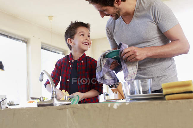 Padre e hijo lavando platos en la cocina - foto de stock