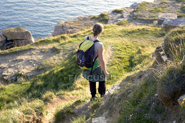 High angle rear view of hiker with backpack hiking down cliff side, Portland, UK — Stock Photo
