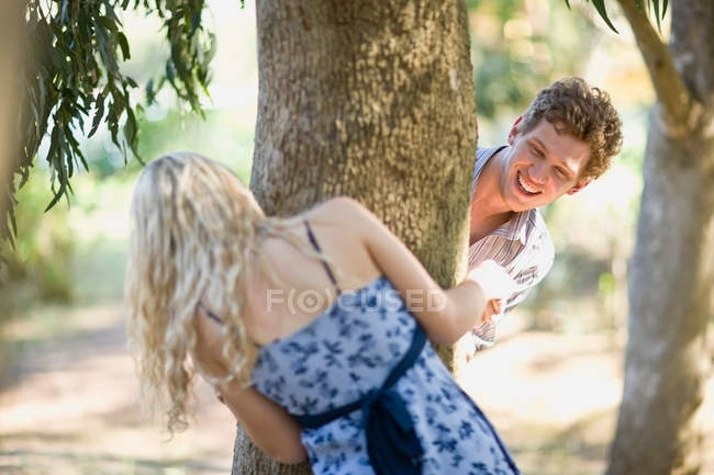 Couple jouant autour du tronc d'arbre — Photo de stock