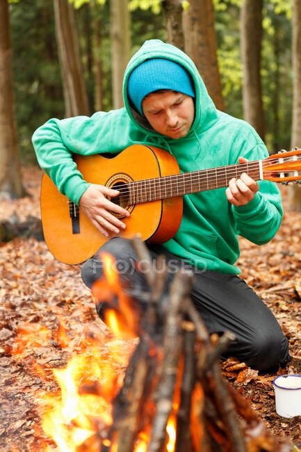 Homme jouant de la guitare par feu de camp — Photo de stock