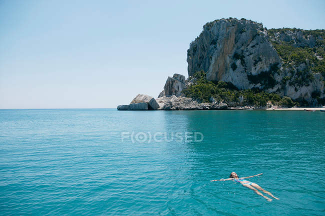 Frau schwimmt in blauer, felsiger Bucht — Stockfoto