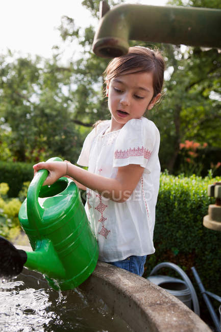 Girl filling up watering can in fountain — Stock Photo