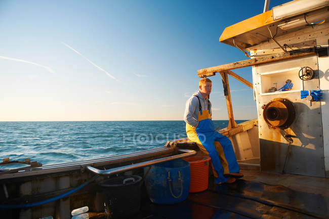 Pescador sentado en la cornisa del barco - foto de stock