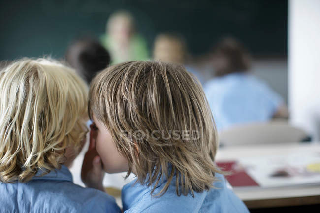 Sussurrando meninos da escola em sala de aula — Fotografia de Stock