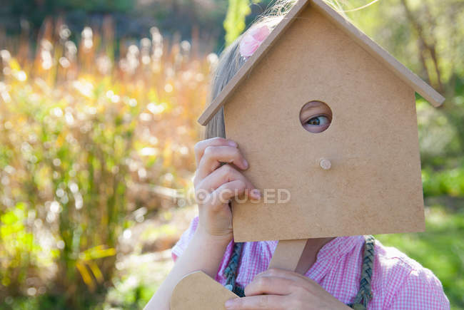 Girl peeking through birdhouse — Stock Photo