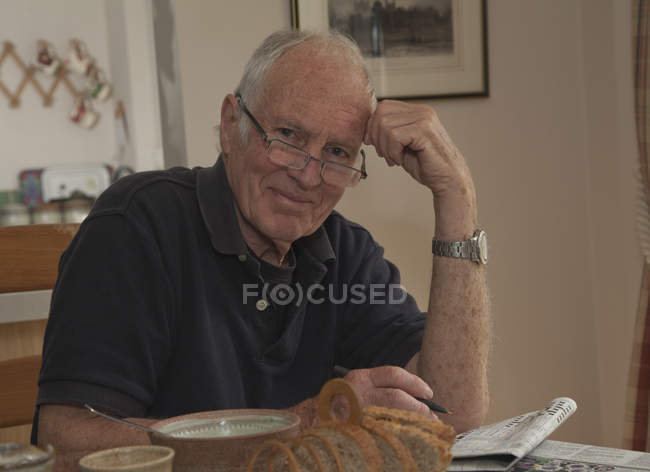 Portrait d'un homme âgé, assis à la table du petit déjeuner avec un journal — Photo de stock