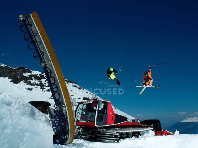 Skiers jumping near piste machine in snow covered mountain hill — Stock Photo