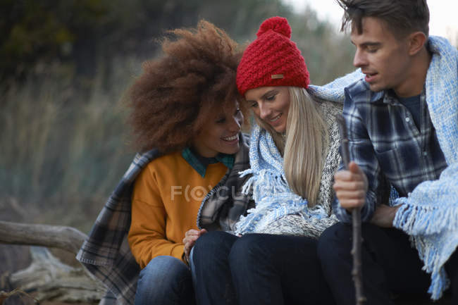 Three adult friends sitting huddled together on beach at dusk — Stock Photo